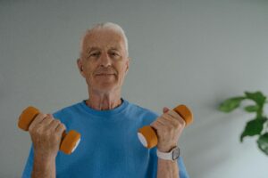 Adulto mayor sosteniendo dos mancuernas naranjas, realizando ejercicio de fuerza.