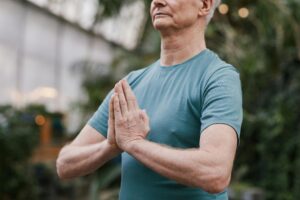 Hombre mayor practicando yoga en interiores, simbolizando bienestar y salud en adultos mayores.
