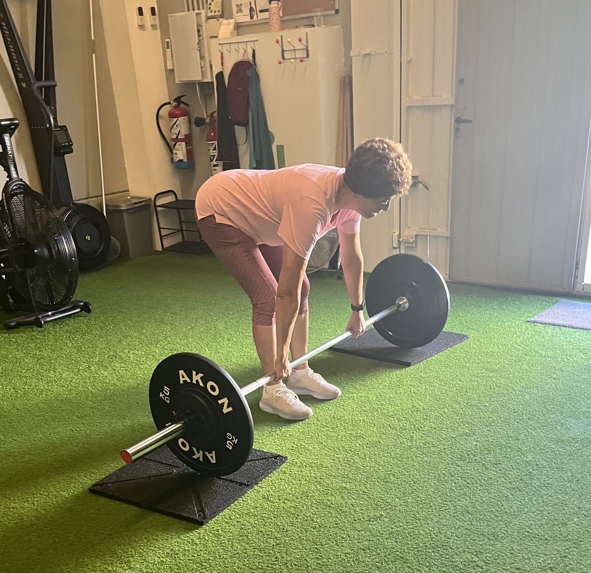 Adulto mayor sujetando una barra con discos en el centro de entrenamiento