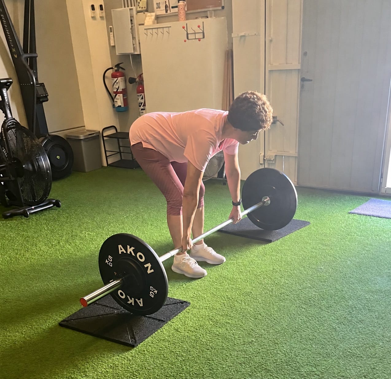Adulto mayor sujetando una barra con discos en el centro de entrenamiento